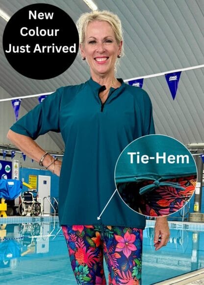 A woman wearing a regular-sized, loose-fit teal rash guard with a neck zipper and adjustable side-tie